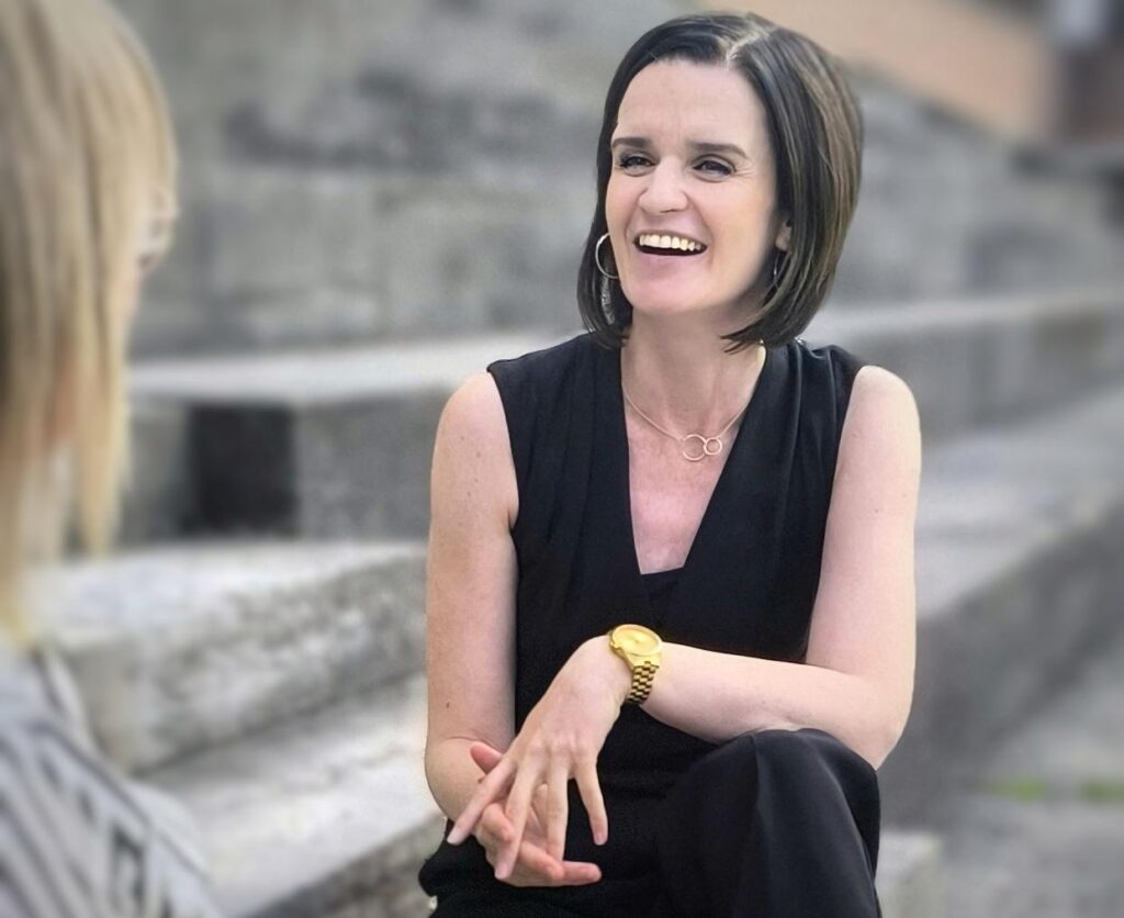 Andrea Heiden lacht und sitzt einer Frau gegenüber.